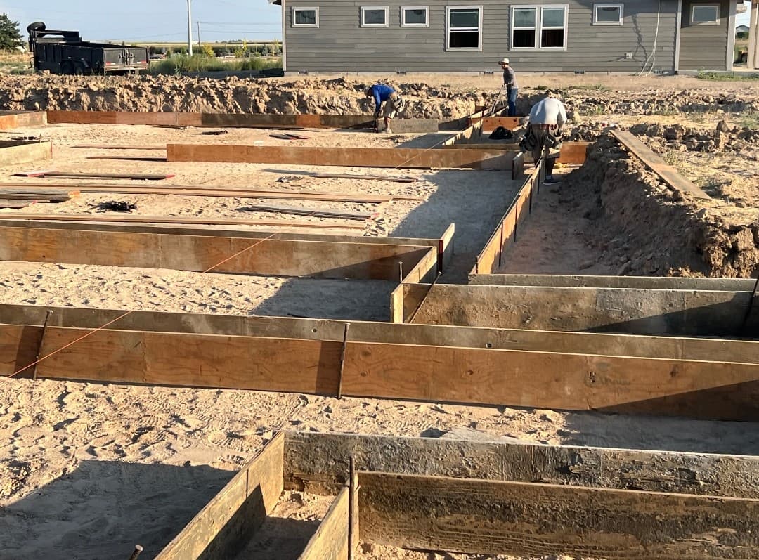 Residential foundation excavation with wooden concrete forms and workers preparing the site